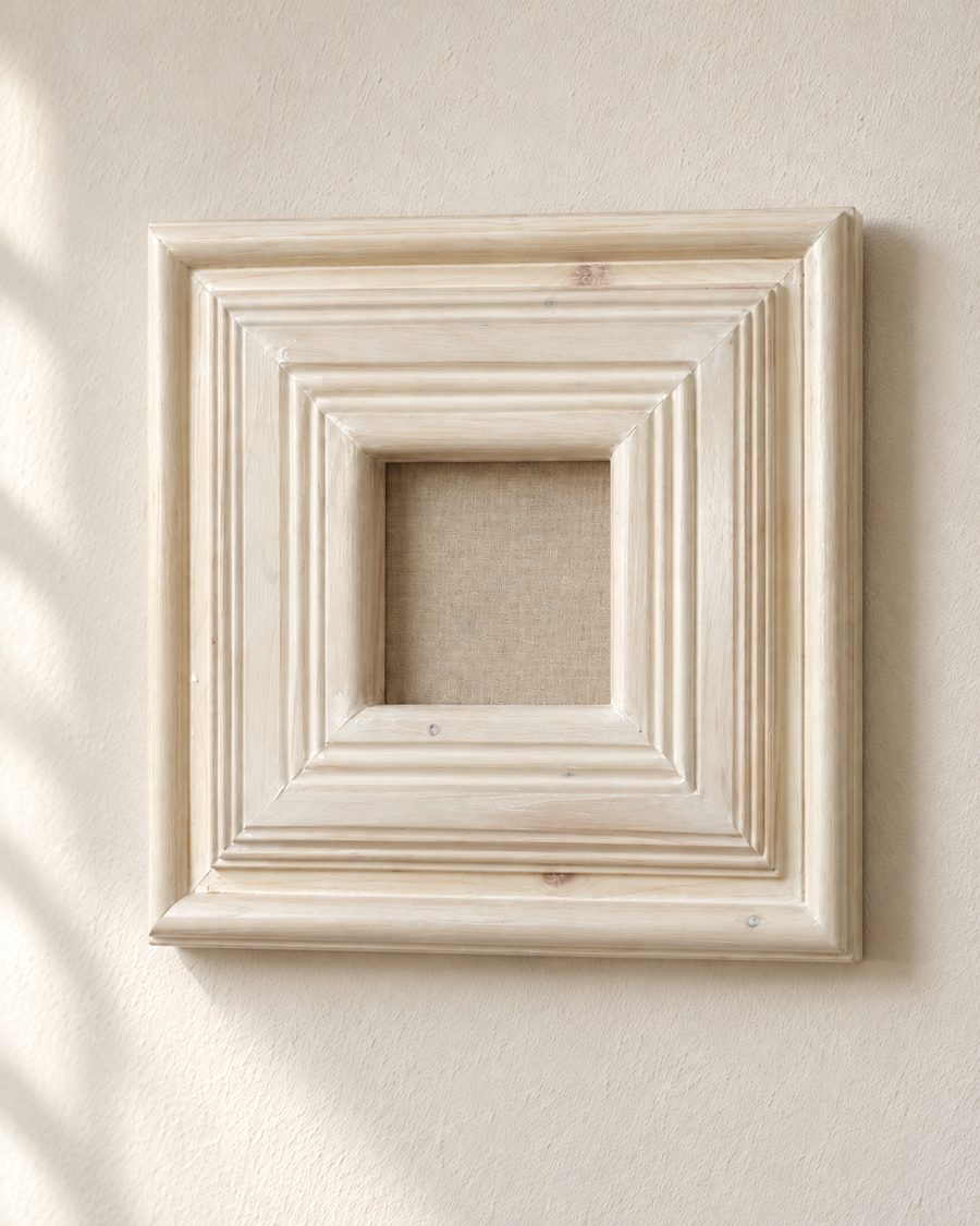 Una grande cornice quadrata a più modanature, sbiancata, appesa a un muro chiaro